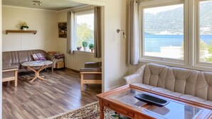 Una sala de estar acogedora con suelo de madera, un sofá de cuero marrón, una mesa de centro de vidrio y vistas a un lago y montañas a través de amplios ventanales.