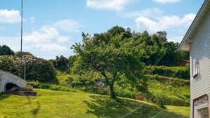 Un césped con un árbol grande, una estructura de piedra y un edificio con techo inclinado.