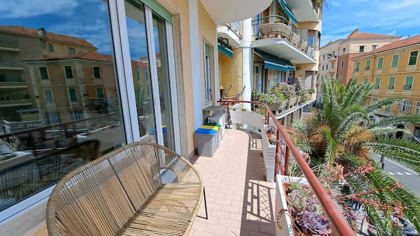 Ein Balkon mit Korbmöbeln, einem kleinen Tisch und Blumentöpfen.