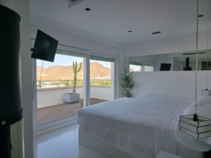 Une chambre moderne avec un grand lit, une télévision et un balcon agrémenté d’un cactus et d’une plante de bambou.