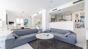 Ein modernes Wohnzimmer mit einem grauen Ecksofa, einem Glastisch und einem dunkelgrauen Teppich.