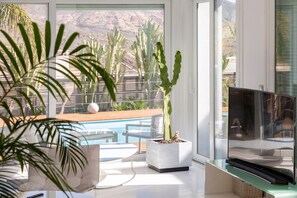Un saló modern amb vista a la piscina, un televisió de pantalla plana i una planta de cactus.