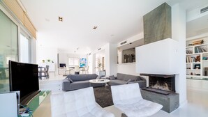 Ein modernes Wohnzimmer mit Kamin, weißen Sofas, einem Flachbildfernseher und einem Essbereich im Hintergrund.