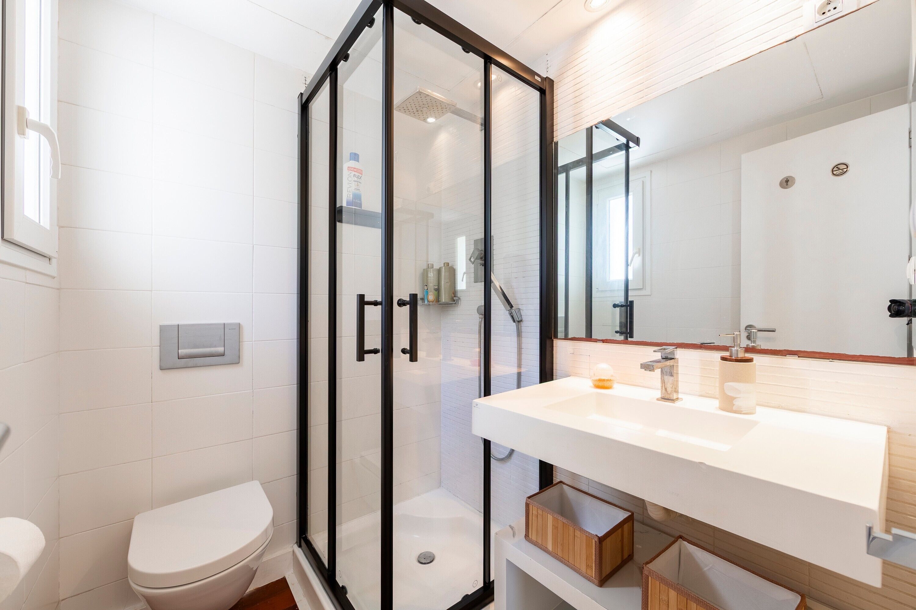 A modern bathroom with a glass-enclosed shower, a white sink with a wooden vanity, and a toilet.