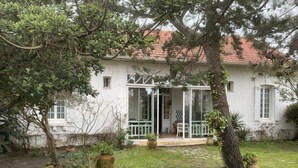 A white house with a glass door entrance, surrounded by potted plants and a small garden area. - 164Gourbets - Belle villa des années 20 pour 14 personnes à Biscarrosse Plage (BISCARROSSE)