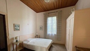 A bedroom with a wooden ceiling, a bed with a white bedspread, a nightstand, a wardrobe, and a window with curtains. - 164Gourbets - Belle villa des années 20 pour 14 personnes à Biscarrosse Plage (BISCARROSSE)