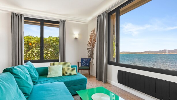 Una sala de estar moderna con un sofá azul verdoso, una mesa de centro verde y un ventanal con vistas al mar y colinas lejanas.