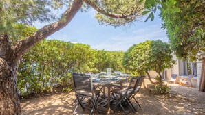 Un área de comedor al aire libre con una mesa redonda y sillas, rodeada de árboles y vistas a un edificio.