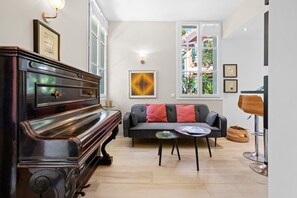 A room with a grand piano, a sofa with cushions, a small round table, and a lamp. - Holiday Home 'Chalet' with Sea View, Wi-Fi and Air Conditioning (Fréjus)