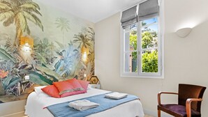 Une chambre à coucher avec un lit, des oreillers, une chaise, une fenêtre et une fresque murale.