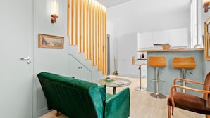 Un intérieur moderne avec un canapé vert, des lambris en bois, une petite table ronde et deux tabourets de bar.