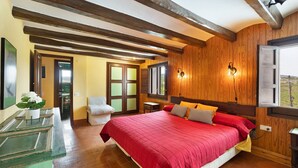 A bedroom with a large bed, wooden ceiling beams, a wooden wall, a window, and a door leading to another room. - Country House 'Cal Eloi Janet' with Mountain Views, Private Pool and Wi-Fi (Sant Marti Sarroca)