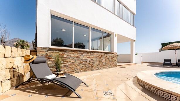 A modern building with a swimming pool, stone wall, and lounge chairs.