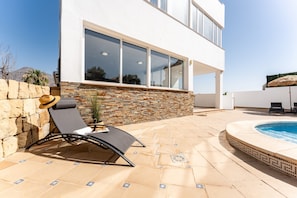 Un bâtiment moderne doté d’une piscine, d’un mur en pierre et de chaises longues.