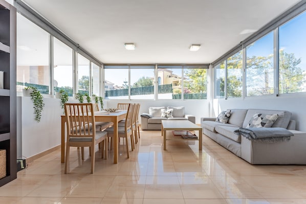 Un vaste espace de vie comprenant une table à manger, des chaises, un canapé et une table basse. De grandes fenêtres offrent une vue sur l’extérieur.