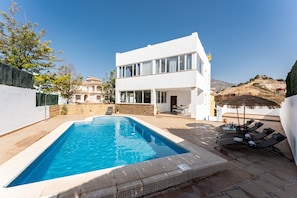 Une maison moderne à deux étages dotée d’une piscine, d’un espace salon extérieur et offrant une vue sur les montagnes.