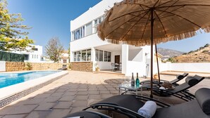 A modern villa with a pool, lounge chairs, and a table with drinks and a hat.