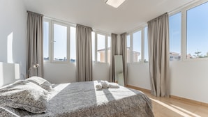 A bedroom with a large bed, a mirror, and multiple windows with curtains.