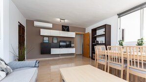 A modern living room with a sofa, TV, dining table, and chairs.