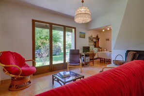 Un salon avec un canapé rouge, un fauteuil en osier, une table basse en verre et un coin repas comprenant une table et des chaises.