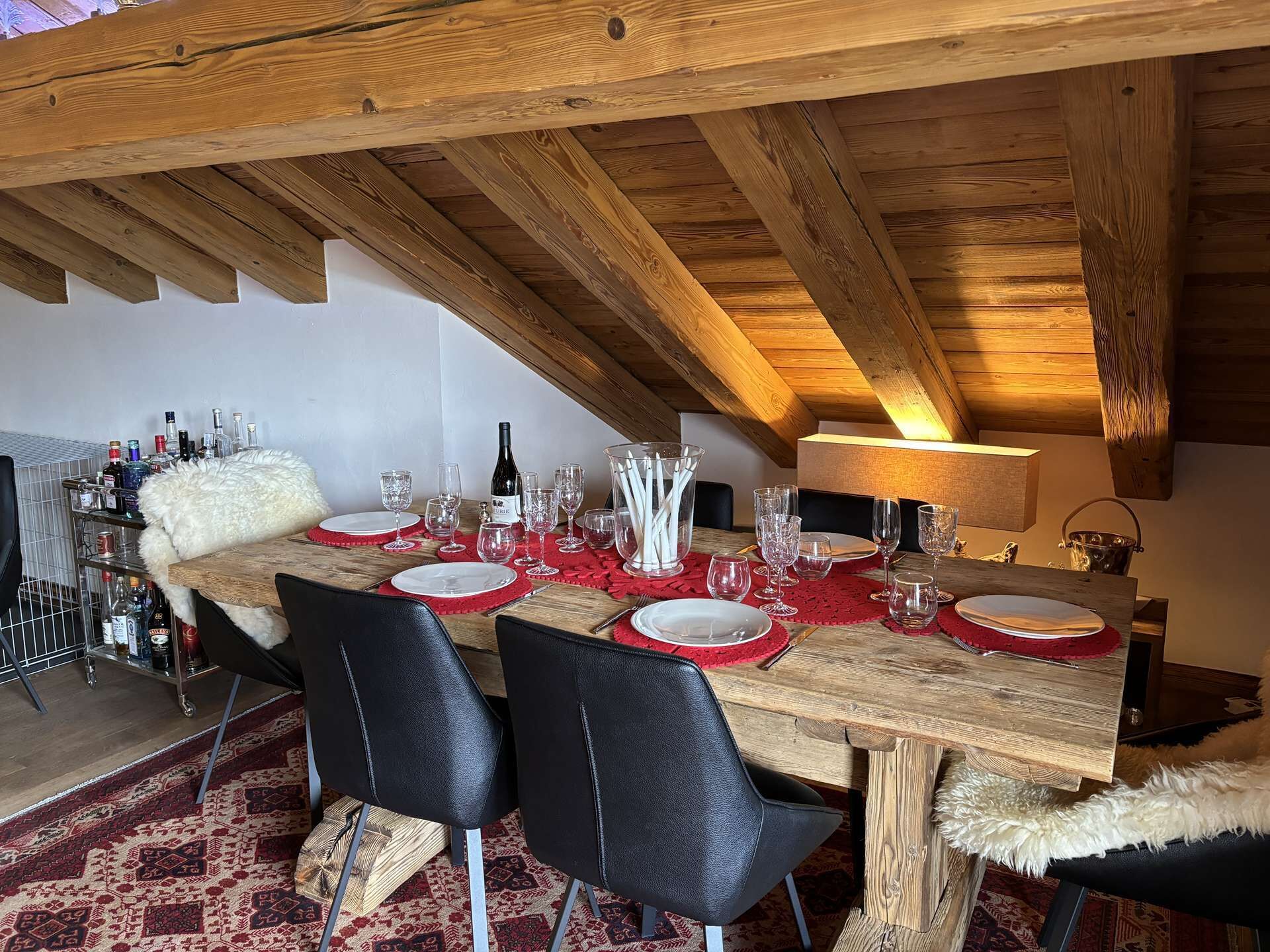 A dining area with a wooden table set for six, black chairs, and a red runner. A white fluffy chair is placed at the end of the table.