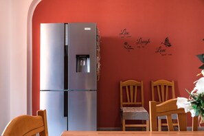 A kitchen with a stainless steel refrigerator, wooden chairs, and a table.