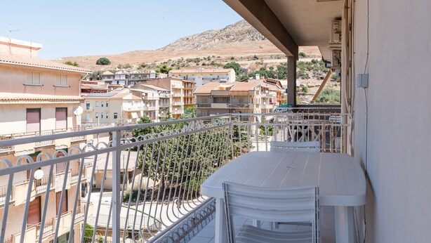 A balcony with a view of a residential area, including buildings and a hill in the background.
