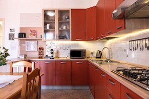 A kitchen with red cabinets, a microwave, a gas stove, and a coffee machine.