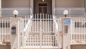 A gated entrance with a staircase leading to a dark doorway, a mailbox, and a sign with a sun and bird.