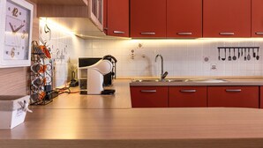 A modern kitchen with red cabinets, a white clock, and a coffee-themed wall.