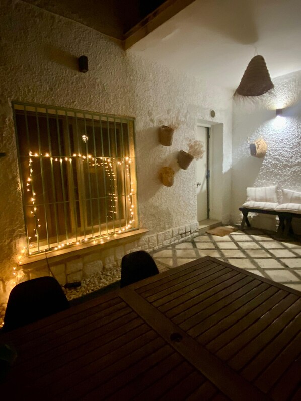 Eine Terrasse mit Tisch und Stühlen, ein Fenster mit dekorativer Beleuchtung und eine Tür mit einem kleinen, an der Wand befestigten Gegenstand.