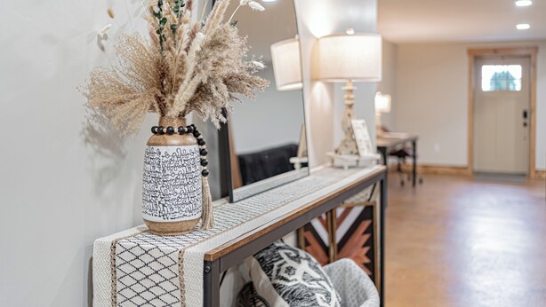 A room with a console table, a mirror, and a vase with dried flowers.