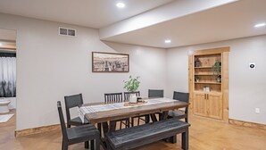 A dining area with a wooden table, six chairs, a bench, a potted plant, and a wooden cabinet with shelves.