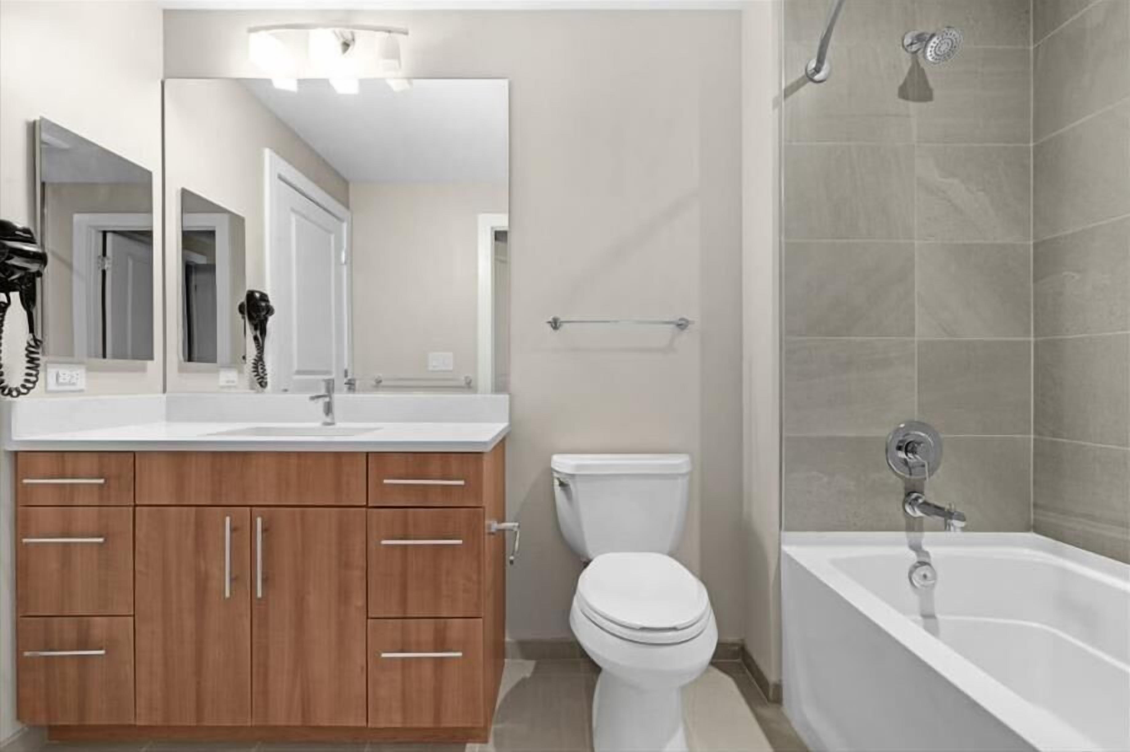A modern bathroom with a white sink, wooden cabinets, a toilet, and a bathtub.