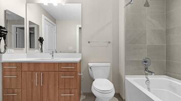 A modern bathroom with a white sink, wooden cabinets, a toilet, and a bathtub.