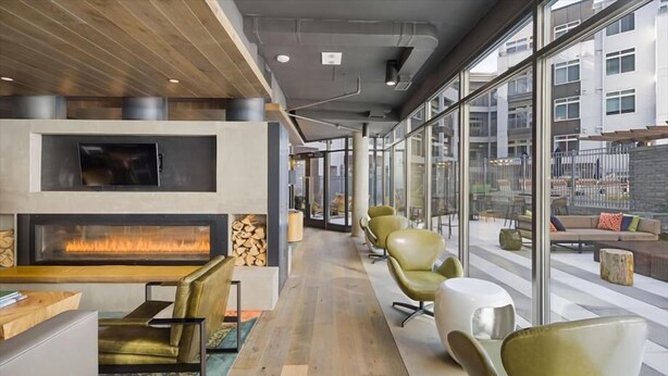 A modern lounge area with a fireplace, comfortable seating, and large windows offering views of the city.