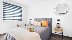Een moderne slaapkamer met een bed, nachtkastjes, een spiegel en een raam met jaloezie ën.