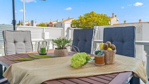 Terras met een eettafel, buitenstoelen, een plant in pot en uitzicht op gebouwen en bomen.