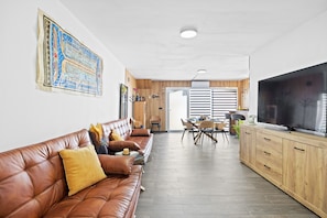 A modern living room with a leather sofa, wooden cabinets, a flat-screen TV, and a dining area with chairs and a table.