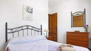 Een bed met hoofdeinde, een houten dressoir, een nachtkastje met lamp en een houten deur.