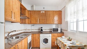 Een keuken met houten kastjes, een wasmachine, een magnetron en een tafel met een ananas tafelkleed.