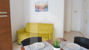 A dining area with a yellow sofa, a table set for two, and a painting on the wall. - Homiday - Felicioni Alba, Two-room apartment on the 1st Floor (Alba Adriatica)