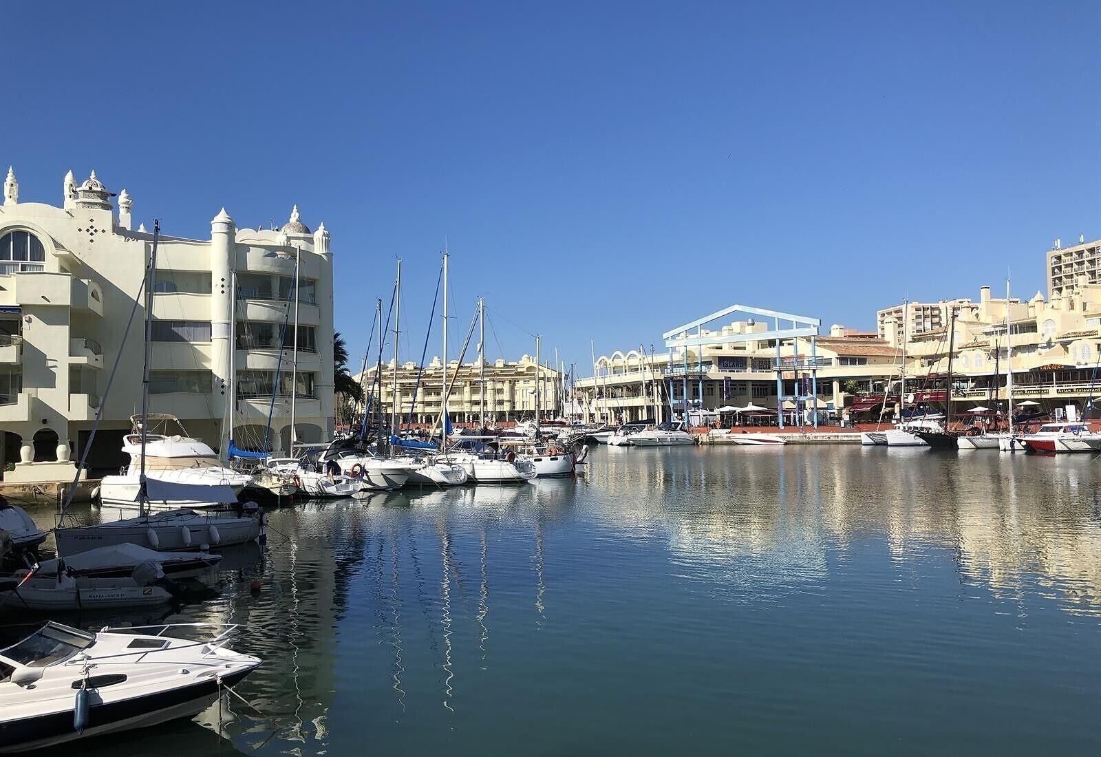 A marina with boats docked, a building with a blue facade, and a white building with balconies.