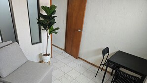 A small room with a grey sofa, a small table with two chairs, a potted plant, and a wooden door. - Singular Reforma (Mexico City)