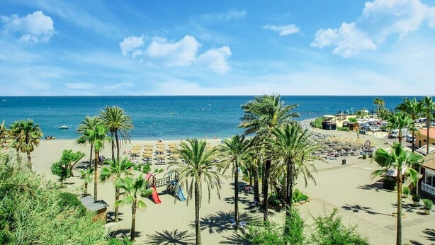 Ein Strand mit Palmen, einem Spielplatz und Blick aufs Meer.