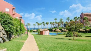 Ein Weg führt zu einem Poolbereich mit Palmen und blauem Himmel.