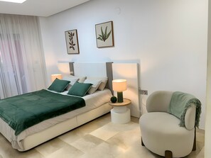 A modern bedroom with a bed, bedside lamps, a chair, and two wall-mounted plant art pieces. - Luxury 100m² Sea View Apartment with Pool, Wi-Fi & Terrace (Benalmádena)
