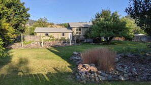 A residential backyard with a stone retaining wall, a lawn, and a house with a sloped roof.
