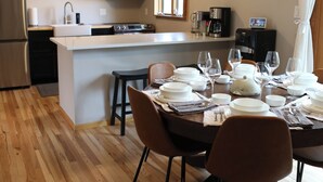 Uma cozinha moderna com ilha central, piso de madeira e área de jantar para seis pessoas, com cadeiras e mesa posta para refeição.