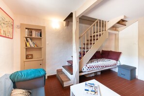 Une pièce avec un escalier, une bibliothèque, un lit recouvert d’une couvre-lit à motifs et une petite table sur laquelle se trouvent divers objets.